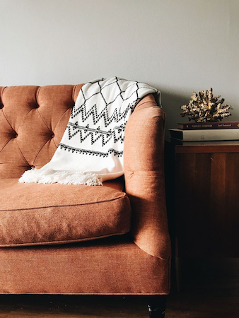 burnt orange sofa button tufted pattern blanket draped coral books side table