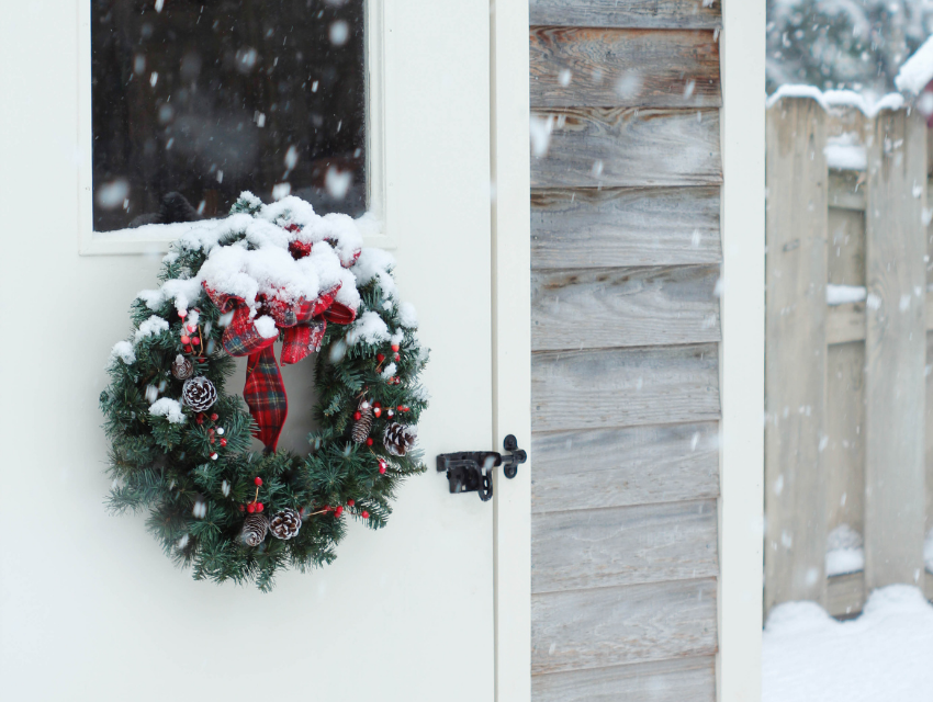 Lakeside-Living_Manitowish-Waters-WI_How-to-Show-Your-Loved-Ones-You-Care-This-Holiday-Season_Wreath-on-White-Door-to-Cabin-in-the-Winter